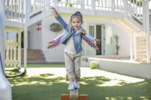 Girls at preschool, portrait balancing on balance beam in garden